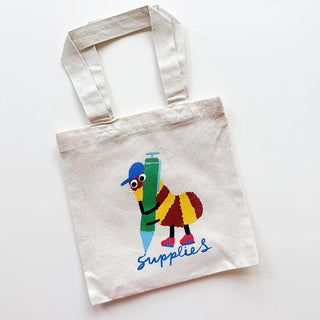 A natural canvas tote bag with a colorful cartoon bug holding a green pencil and the word 'Supplies' printed in blue script, shown on a plain white background.