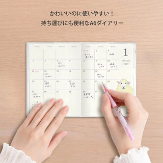 A6 monthly planner open on a desk with hand holding a pen writing