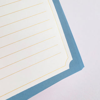 Close-up of lined paper with blue border and gold foil pages on a light gray background
