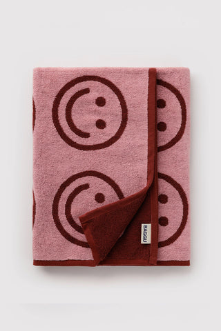 Folded blush bath towel with smiley-face print and attached woven label