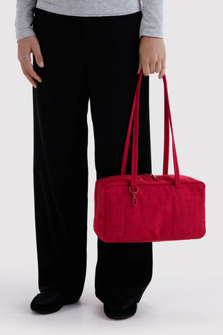 Red nylon bowler bag held at side, showing top handles and zippered front