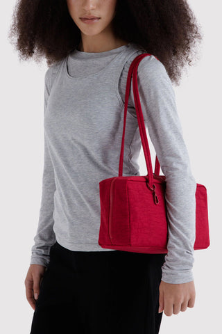 Red nylon bowler bag worn cross-body style with top handles and zip pocket