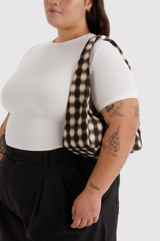 Person wearing a white t-shirt and black pants with a checkered bag over one shoulder on a white background