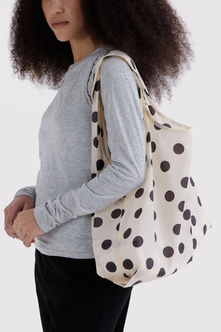 Cream polka dot tote bag with black spots, held over shoulder by long straps