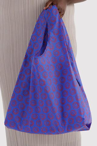 BAGGU mini tote bag held open in cobalt blue with red smiley circle pattern