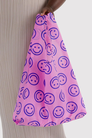 Pink standard tote bag with large smiley face icons, held by one hand