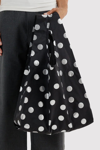 Black tote bag with silver polka dots, held by the wide handles