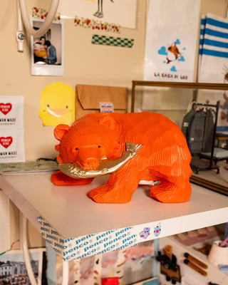 Orange bear coin bank with fish in its mouth on a shelf