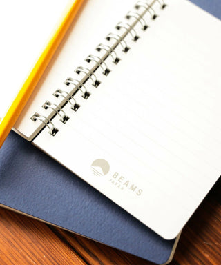 Notebook with spiral binding on a wooden surface, featuring the 'Beams' brand.