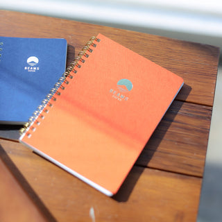 Two notebooks, one blue and one orange, on a wooden surface.