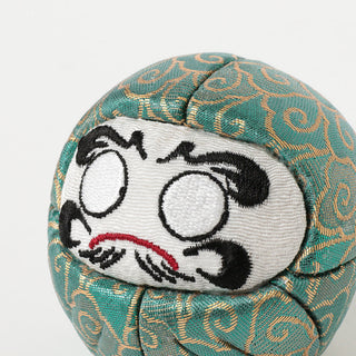Decorative daruma with embroidered face on a green fabric background