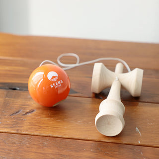 Orange kendama ball with a white string and wooden handle on a wooden surface.