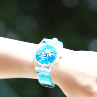 Person wearing a blue watch with a mountain design on a blurred green background