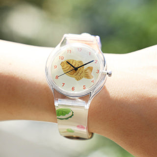Wristwatch with a fish design on the dial worn on a wrist against a blurred green background