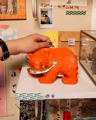Hand putting coin in back of wooden carved bear coin bank