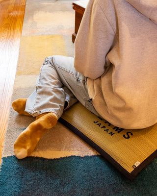 Person wearing a hoodie and light blue jeans sitting on a cushion