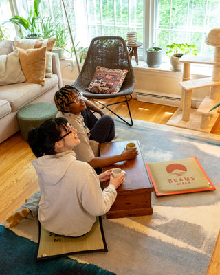 Two people sitting on a rug in a cozy living room with a coffee table and decorative items.