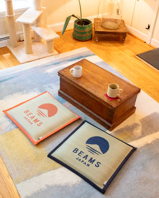 Two 'Beams Japan' branded mats on a rug with a wooden coffee table and cups in the background.