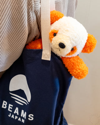 Navy blue bag with a logo and a small orange and white plush toy on a neutral background