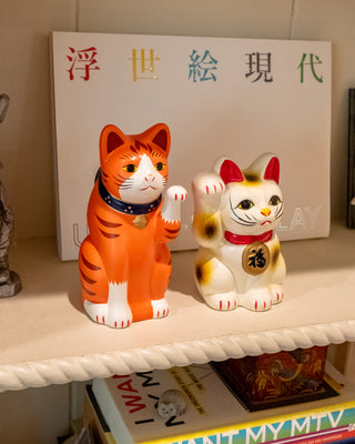 Two ceramic cat figurines on a shelf with a book in the background