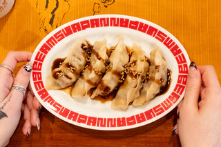 Dumplings with a dark sauce on a plate with red text, held by two hands.