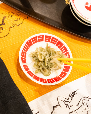 Seaweed with chopsticks on a branded beams plate with orange cloth and black tray in the background.