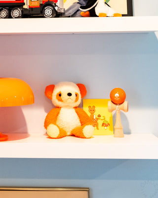 Shelf with a teddy bear, lamp, and wooden kendama toy against a light blue wall.
