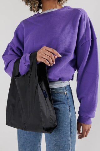 Black Baby BAGGU tote bag with blue logo patch, carried by strap