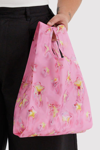 Pink reusable bag with star pattern held by a person wearing black pants.