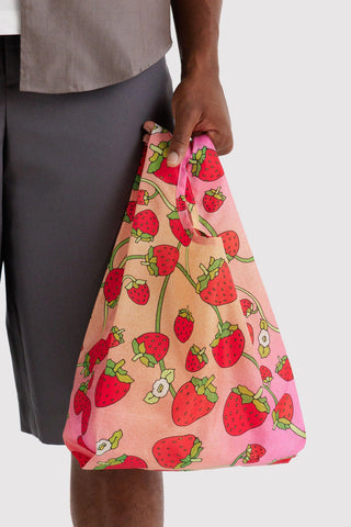 Baby BAGGU strawberry-print reusable tote bag held by handle, pink with red strawberries.