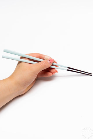 Hand holding light blue bamboo chopsticks against a white background