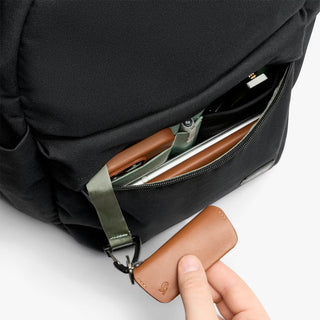 Black backpack with front pocket open and small items inside. Hand pulling out keychain attached to inside of backpack