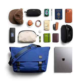 Collection of travel items surrounding a blue messenger bag to show capacity