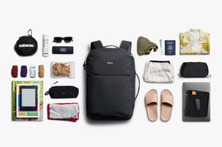 Black backpack with various travel items arranged around it on a white background