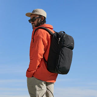 Person wearing an orange jacket and black backpack against a clear blue sky