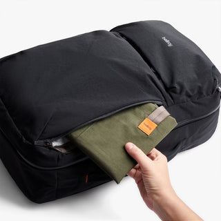 Person taking out a green folded back of a a black backpack on a white background