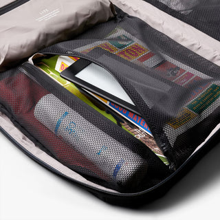 Mesh pouch with travel essentials including a book and toiletries on a white background