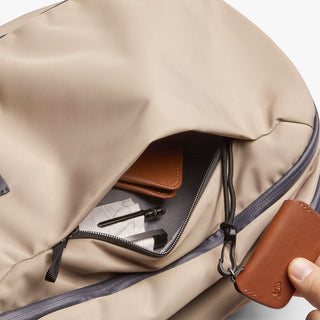 Beige backpack with a brown leather wallet inside and hand holding keychain attatched