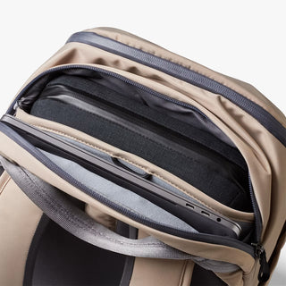 Close-up of a beige backpack interior with an open zip compartment, showing gray and black padded compartments and zipper details.