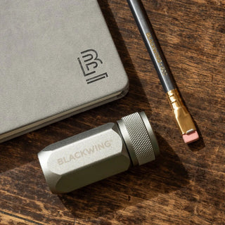 Blackwing pencil and eraser on a wooden surface with a notebook.