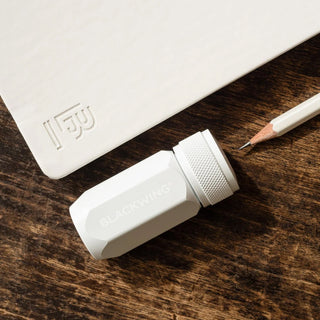 White mechanical pencil sharpener on a wooden surface with a pencil and a white container.