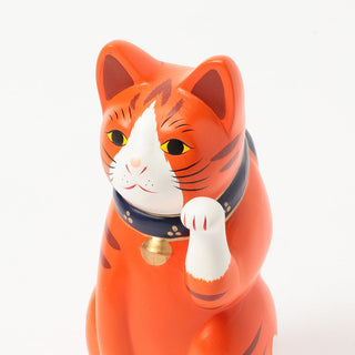 Orange cat-shaped figurine with a collar  and its paw up on a white background