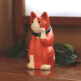 Orange cat figurine with a collar on a wooden surface with plants in the background