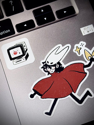 Laptop with stickers on a keyboard, including a cartoon character and a retro computer design.