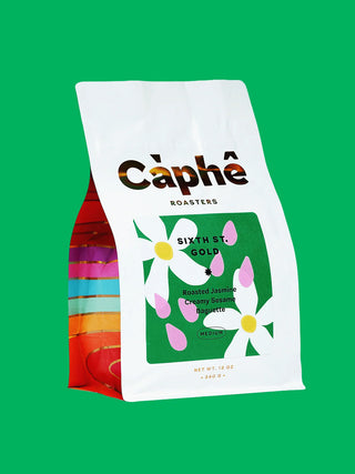 A bag of Caphe Roasterse Sixth Street Gold medium roast coffee on a green background. The packaging features florals