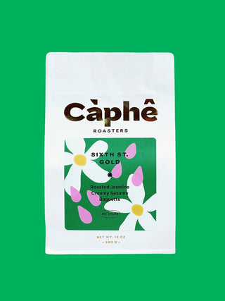 A white bag of Câphé Roasters Sixth St. Gold coffee on a solid green background.
