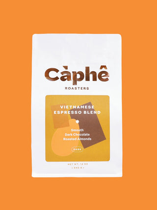 A white bag of Câphé Roasters Vietnamese Espresso Blend coffee, featuring a gold and brown graphic label, centered on a solid orange background.
