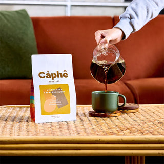A person pouring coffee on a table in a living room setting with Caphe Roasters Vietnamese Espresso blend bag of coffee on the table