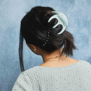 Octopus claw hair clip on dark straight hair, light blue translucent with curved prongs.