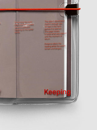 Close-up of a clear notebook cover taupe-brown notebook, a red elastic band across the top, and red printed text on the side. The word 'Keeping' is overlaid in red near the bottom.